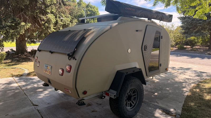  arid landscape.|Adventure ready: A truck tows an Escapod teardrop RV rental on golden grass. Rocky bluffs and a boy walking complete the scene.|This rugged tan teardrop camper — photo 9