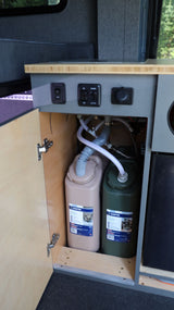 RV rental: Camper van interior showing water tanks (fresh/grey), plumbing, and control panel with wood countertop.
