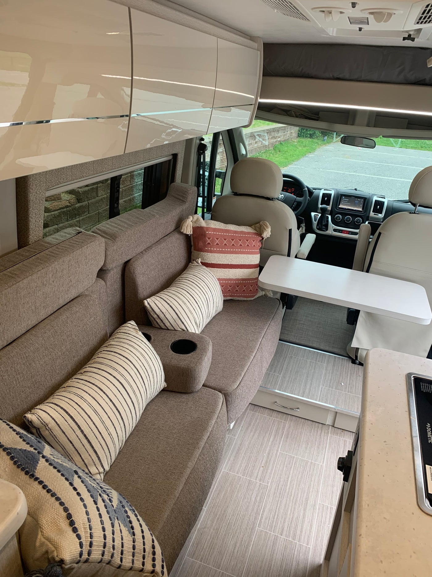 Inside a sleek rv rental: a comfy living space with throw pillows, glossy cabinets, and front cockpit area. — photo 12