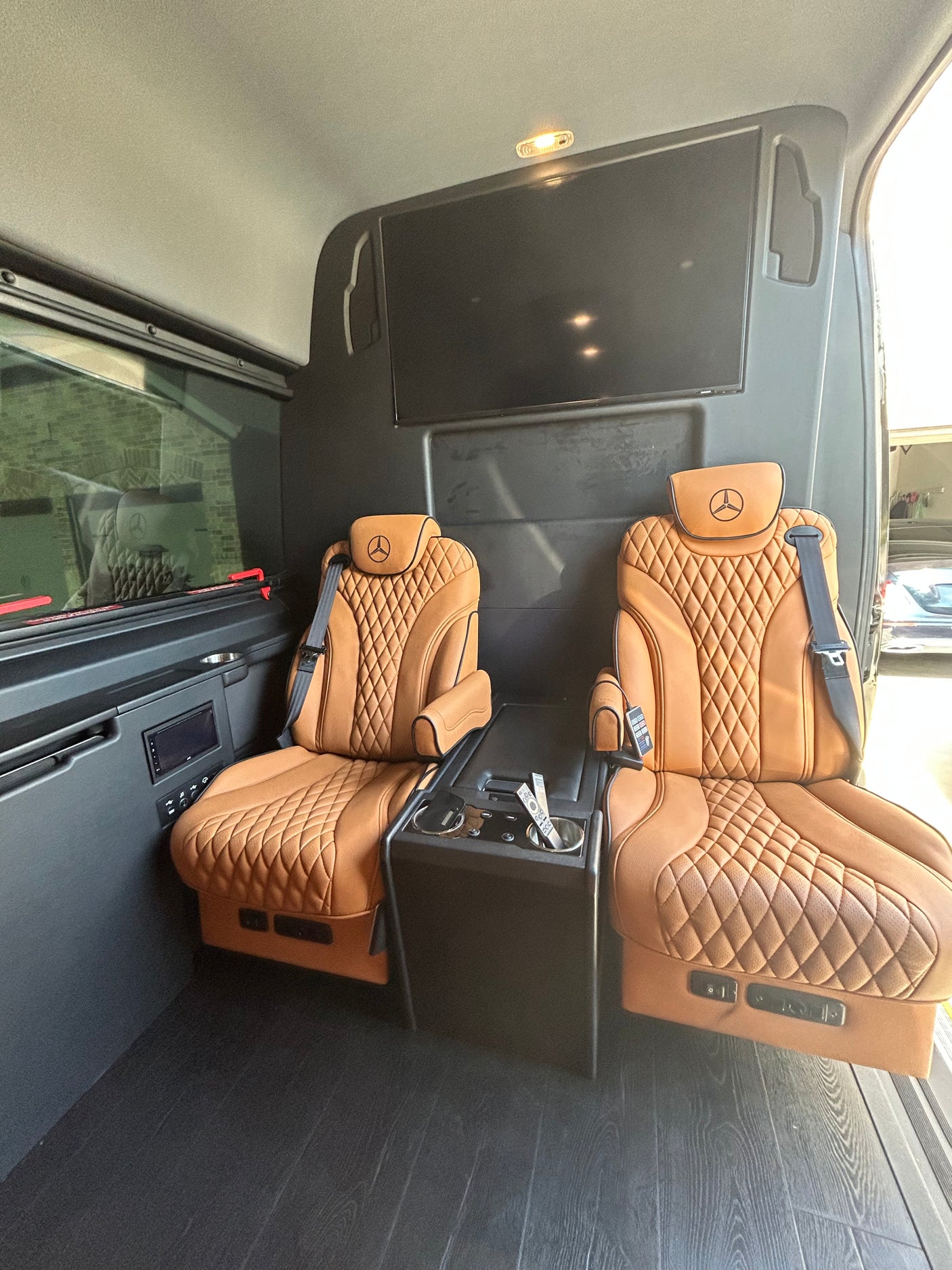 Luxury rv rental interior: plush quilted leather captain's chairs, TV, and console offer premium comfort for travel.