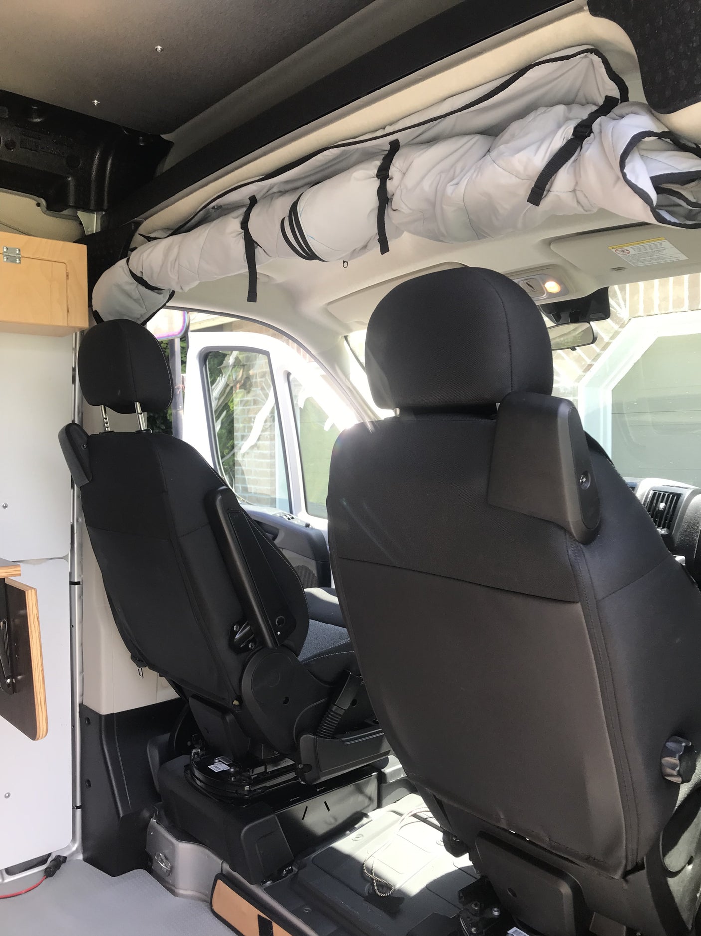 RV rental interior with black front seats, one swiveled, and overhead rolled storage, ideal for van life adventures.