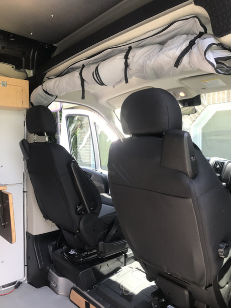 RV rental interior with black front seats, one swiveled, and overhead rolled storage, ideal for van life adventures.