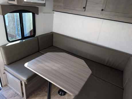 RV rental dinette featuring comfortable U-shaped seating, a wood-grain table, and a sunlit window.