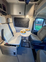 Cozy RV rental interior features a dinette table with food, front seats, and two passenger seats, ideal for travel.