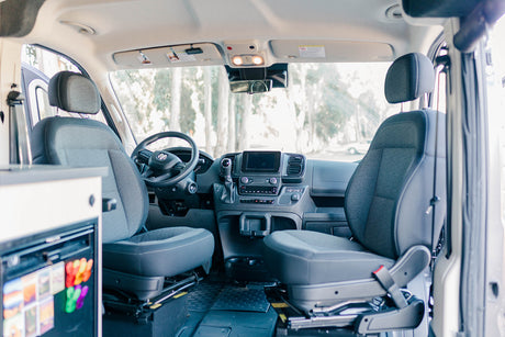 Inside this RV rental: A detailed view of the front cabin with driver and passenger seats, dashboard, and built-in fridge.