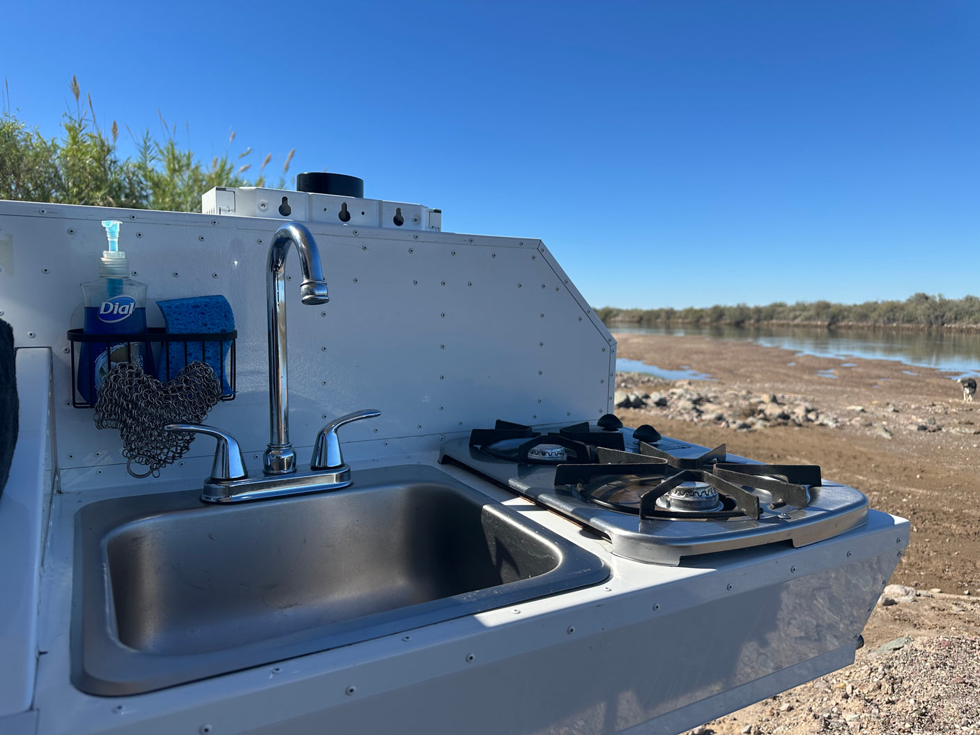 This RV rental's outdoor kitchen features a sink, faucet, and dual-burner stove, perfect for cooking by the river.
