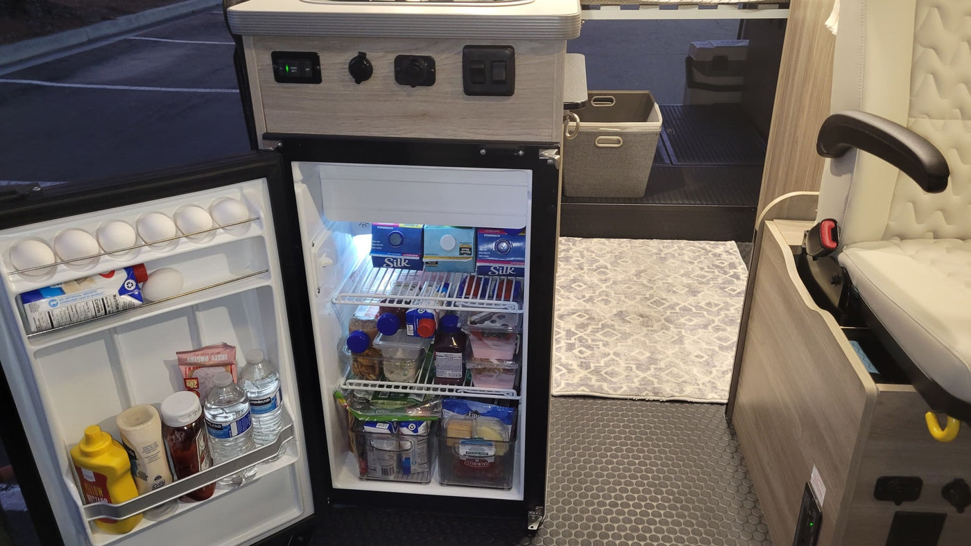 Open fridge in an RV rental reveals food, drinks, and organized storage. A glimpse of the camper's cozy interior. — photo 7