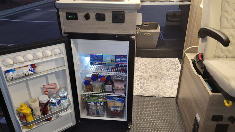 Open fridge in an RV rental reveals food, drinks, and organized storage. A glimpse of the camper's cozy interior. — photo 7
