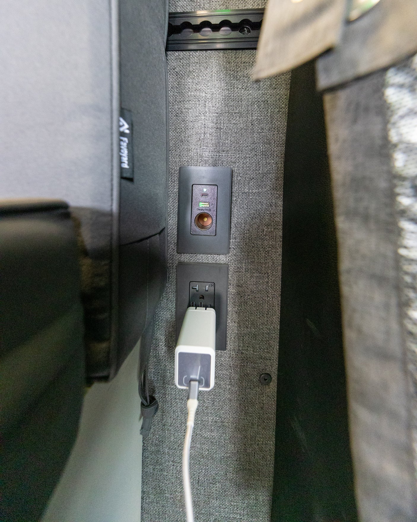 Modern RV rental charging hub: USB-C, USB-A, 12V, and AC outlet with a charger plugged into a gray textured wall.