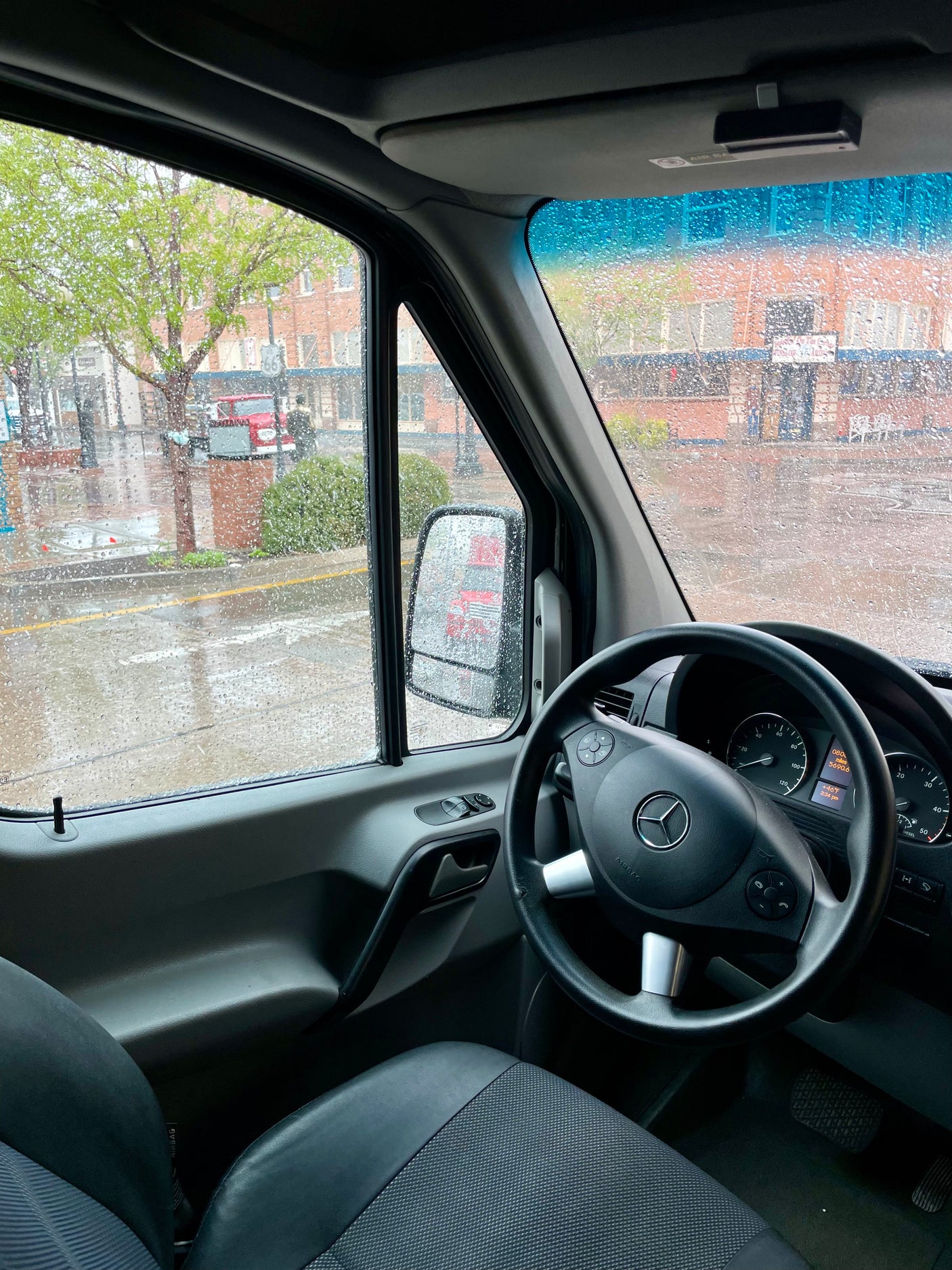 Rainy view from a Mercedes-Benz Sprinter rv rental van interior. Raindrops cover the windows, dashboard with mileage visible.