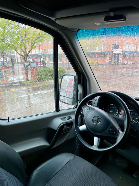 Rainy view from a Mercedes-Benz Sprinter rv rental van interior. Raindrops cover the windows, dashboard with mileage visible.