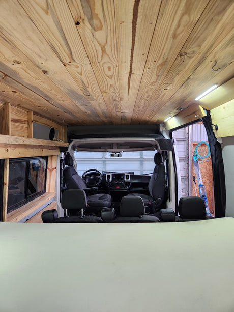 Wood-paneled camper van interior, featuring ceiling, bed, & front cabin. Ideal for RV rental trips.