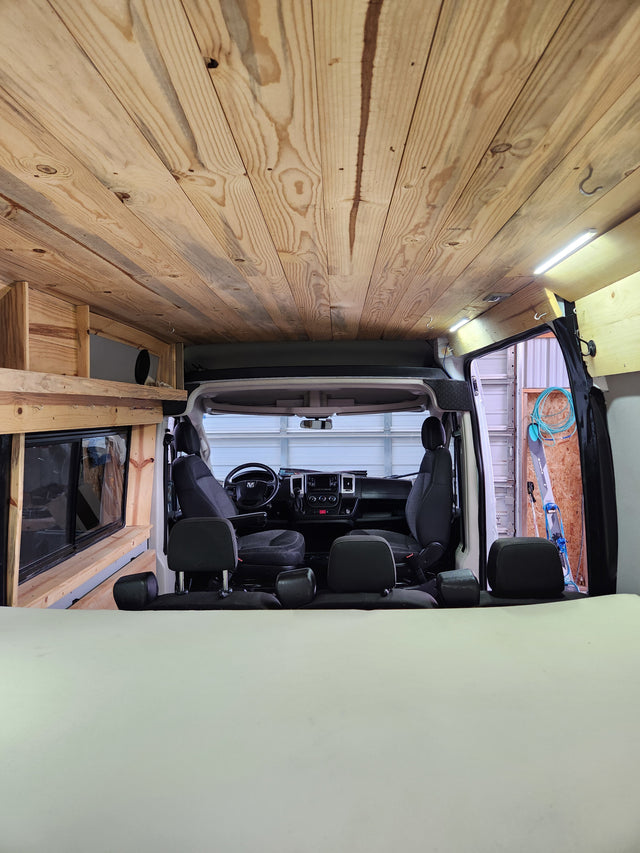 Wood-paneled camper van interior, featuring ceiling, bed, & front cabin. Ideal for RV rental trips.