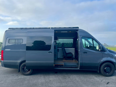 Gray Mercedes Sprinter camper van, great for RV rental, with side door open revealing custom interior. Ready for your travels.