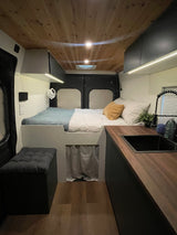RV rental interior: a cozy bed, sleek kitchenette with sink, and warm wooden ceiling create a comfortable space.