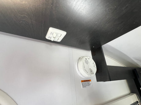 Inside an RV rental: Ceiling and porch light switches, plus a critical smoke alarm with warning label for safety.
