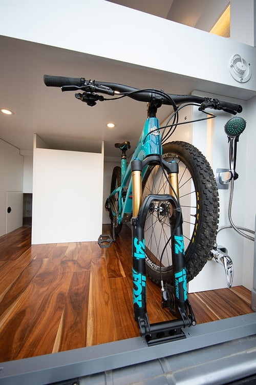 Inside an **rv rental**: a turquoise mountain bike is secured via its front fork on the wooden floor, next to a functional shower setup.