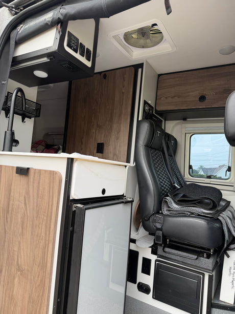 Interior of a well-equipped rv rental: kitchenette with sink/faucet, fridge, overhead controls, and a comfy passenger seat.