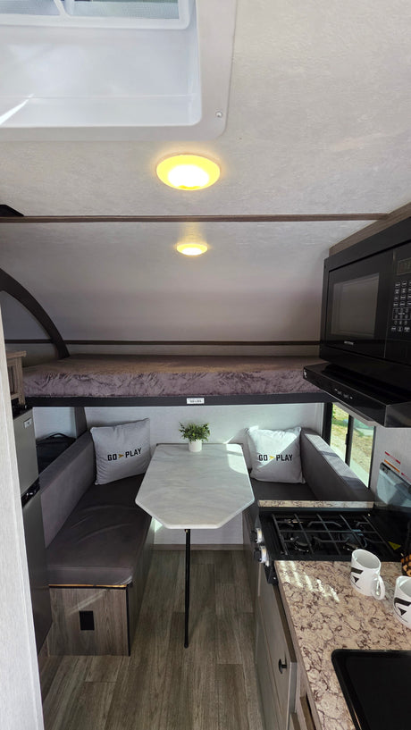 Compact RV rental interior: kitchen, dinette with "Go Play" pillows, and an overhead bunk bed. Perfect for travel!