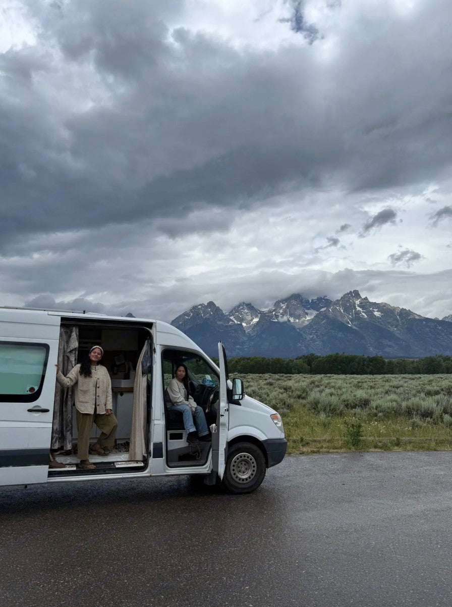 RV rental adventure with two women and their camper van against majestic mountains under cloudy skies.