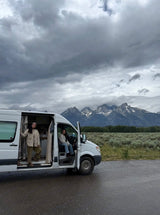 RV rental adventure with two women and their camper van against majestic mountains under cloudy skies.