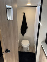 Inside an RV rental bathroom: a white toilet, black towel, shower curtain, and a mirror on the door. Compact and functional.