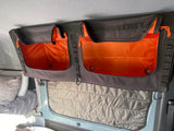 RV rental overhead storage pockets with bright orange interiors and quilted window insulation visible inside a camper.