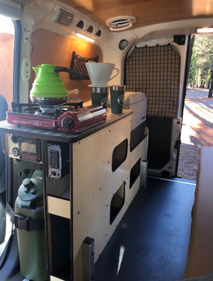  showing its cozy interior. Ideal for an RV rental forest camping trip.|Illuminated camper van interior visible with rear doors open — photo 8