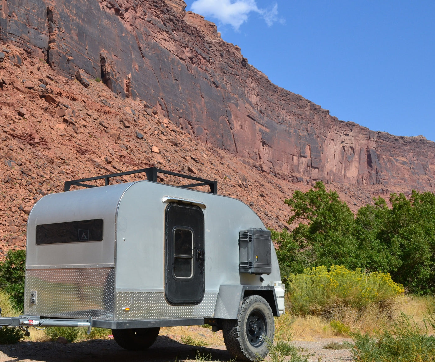 This rugged off-road camper trailer, ideal for an RV rental adventure, is parked against a huge red rock cliff. — photo 10