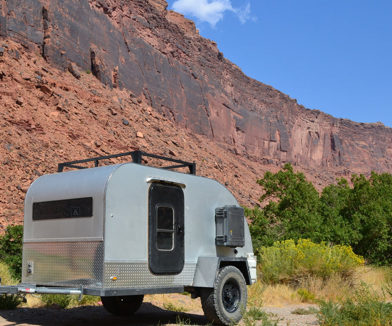 This rugged off-road camper trailer, ideal for an RV rental adventure, is parked against a huge red rock cliff. — photo 10