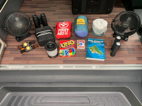 RV rental ready with essential camping gear: fans, lights, first aid, binoculars, games, and an Oahu travel guide.