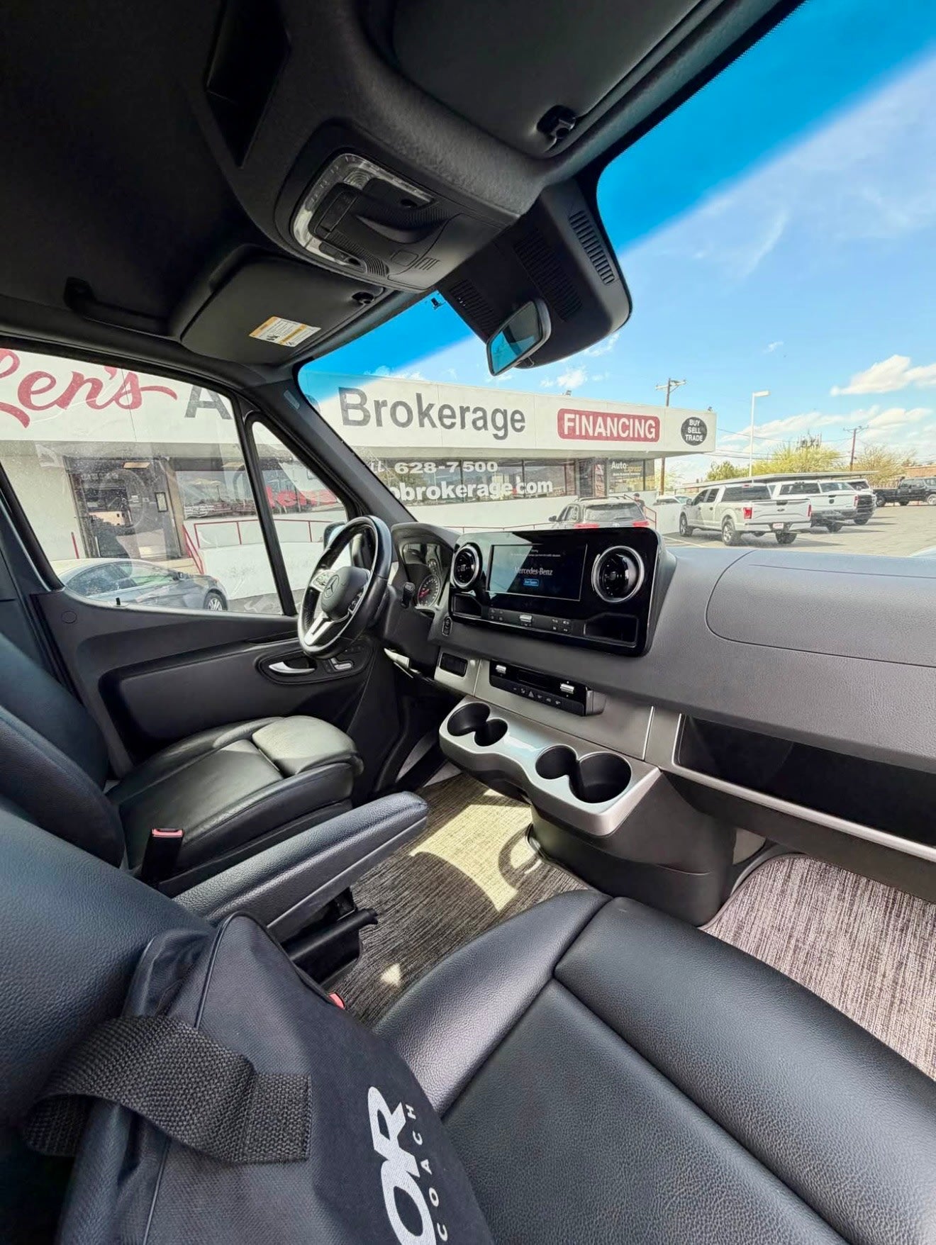 Modern RV rental van interior: Sleek dashboard, black leather seats. Parked outside a vehicle brokerage offering financing.