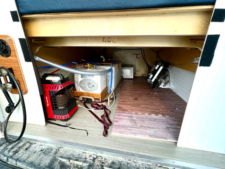 RV rental camper van interior: under-bed storage with Bosch water heater, Mr. Heater, and utility plumbing.