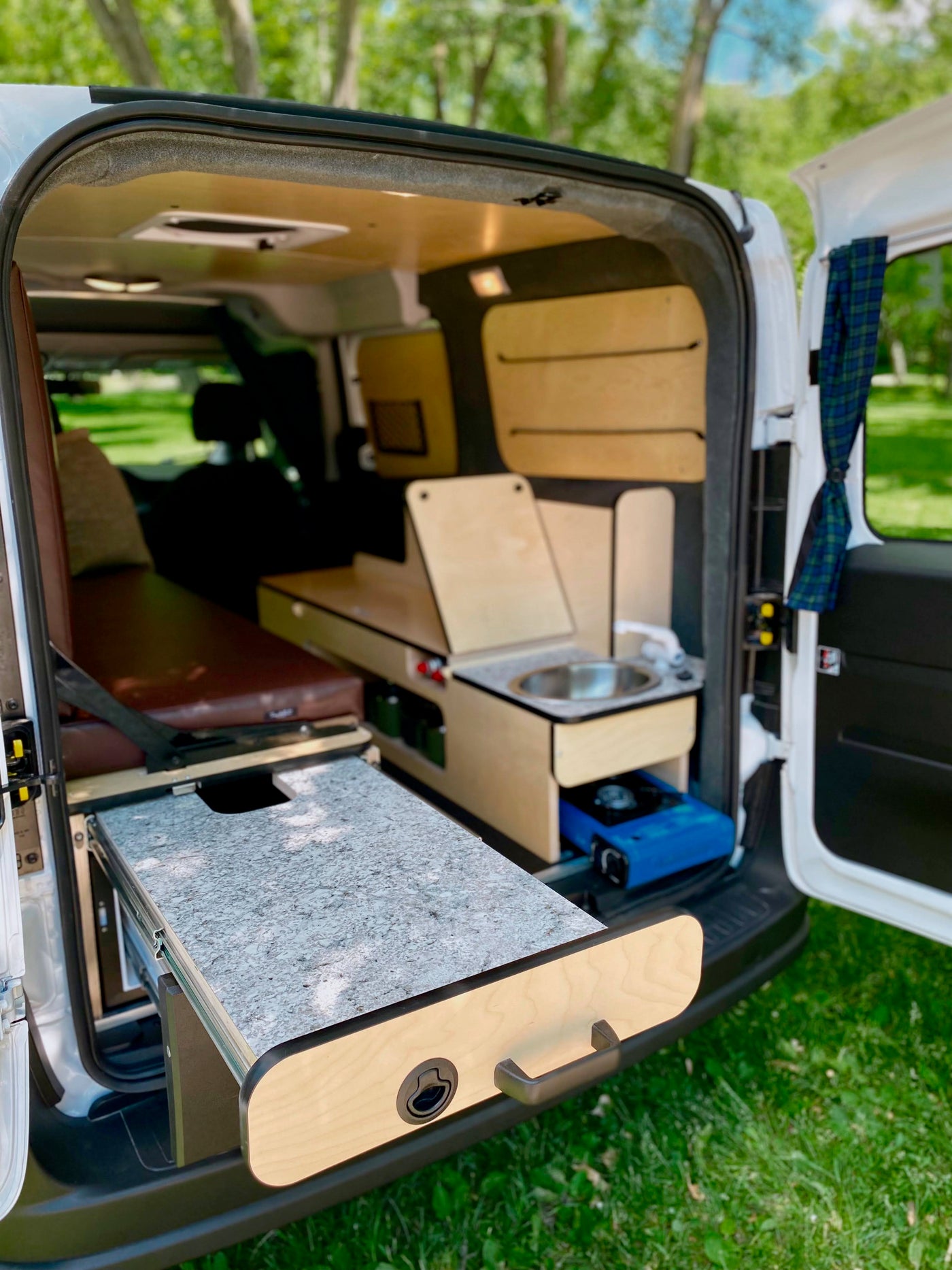 RV rental: Inside a custom camper van with bed, integrated sink, and pull-out kitchen counter for outdoor cooking. — photo 7