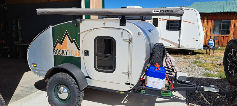 This teardrop RV rental features an ARB awning and adventure gear. A larger travel trailer and building are in the background. — photo 9