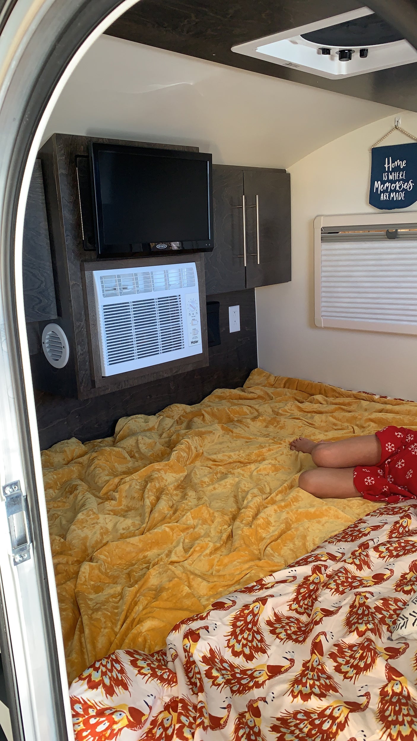 Cozy RV rental interior with a comfy bed, TV, AC, and a person relaxing. Great for travel!