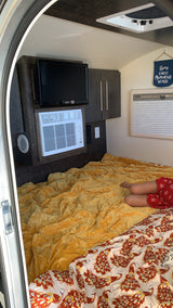 Cozy RV rental interior with a comfy bed, TV, AC, and a person relaxing. Great for travel!