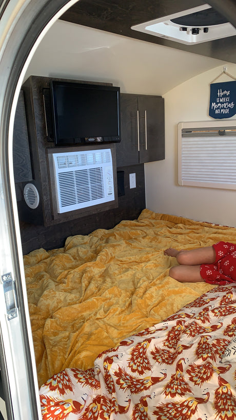 Cozy RV rental interior with a comfy bed, TV, AC, and a person relaxing. Great for travel!