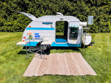 This Retro Jr. teardrop RV rental offers a perfect camping retreat with an outdoor kitchen, picnic area, and patterned rug.