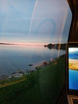 Serene lake sunset viewed from an RV rental window, showing interior reflections and a laptop. Ideal for scenic travel.