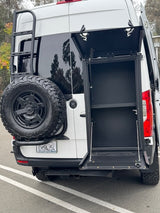 Open rear storage cabinet on this rv rental, with a spare tire and ladder, ready for adventure trips.