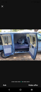 Light blue conversion van's spacious interior for RV rental. Features plush blue carpet & swivel armchair with side doors open.