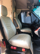 Inside an RV rental: light-colored front driver and passenger seats of a camper van, with dashboard & living area view.