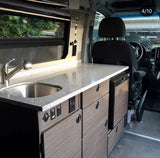 Compact RV rental interior featuring a modern kitchenette with sink, integrated fridge, and sleek cabinetry for mobile living.