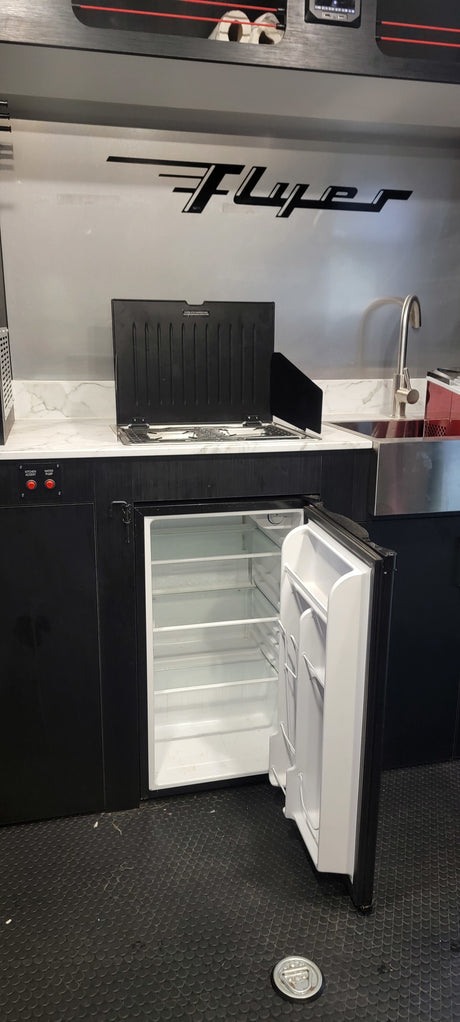 Ready for adventure: an RV rental's functional kitchen with sink, stove, and an empty fridge waiting to be stocked.