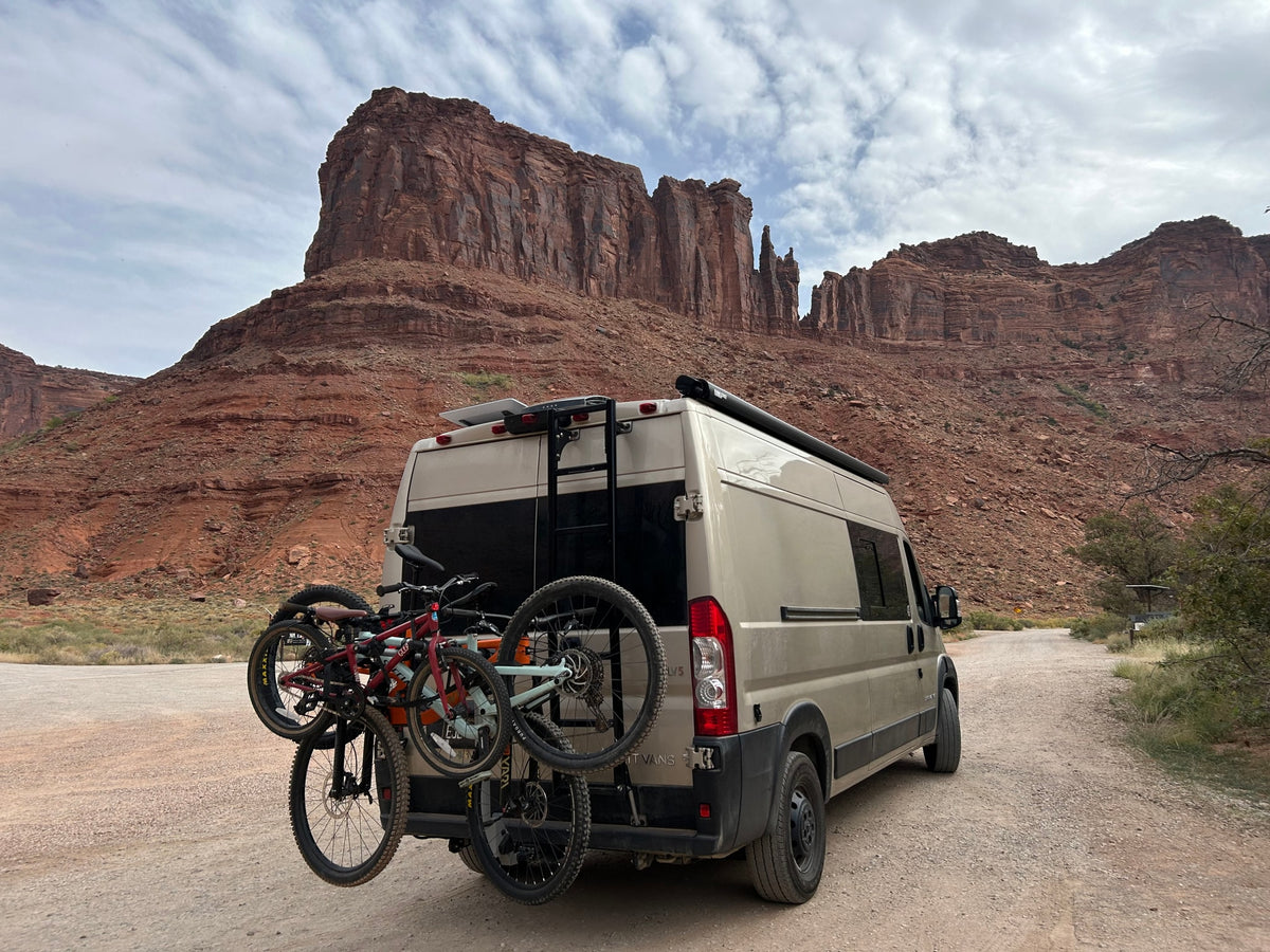 An adventure-ready RV rental with bikes attached, set against majestic red rock formations under a cloudy sky. — photo 8