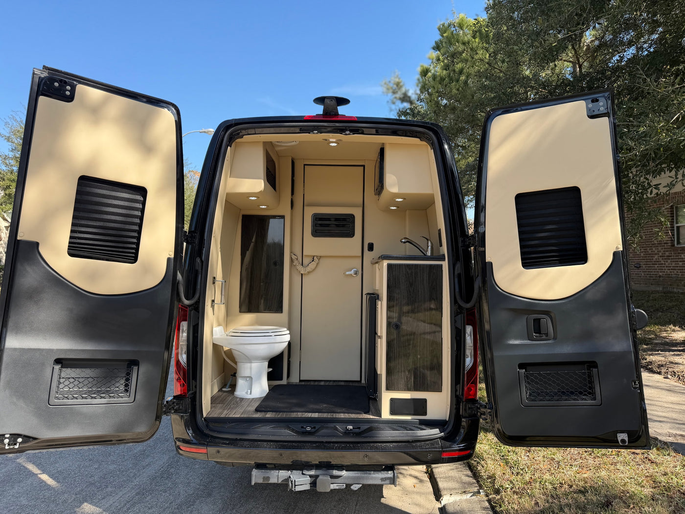 Rear view of an rv rental camper van, doors open, revealing a compact interior with a toilet, sink, and cabinets. — photo 14