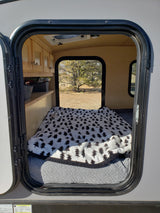 Cozy rv rental interior: A compact camper with a bed, tree-patterned blanket, cabinets, and a window view of nature.