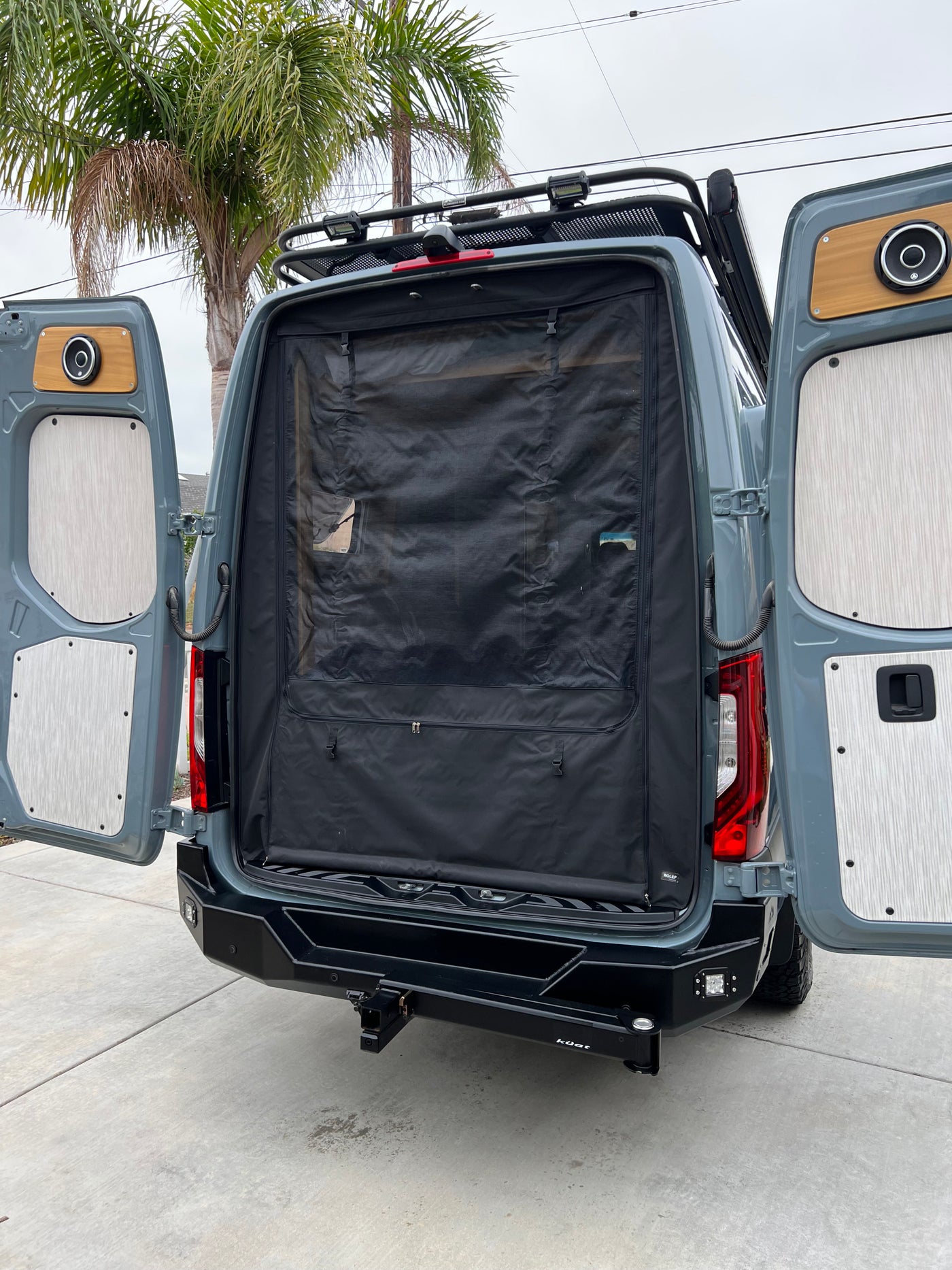 RV rental ready: rear view of a custom camper van with open doors, bug screen, roof rack, and heavy-duty bumper. — photo 10