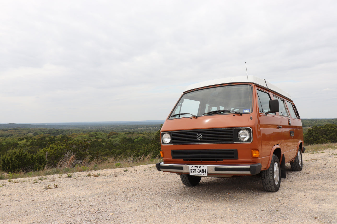 This orange VW Vanagon high-top camper is perfect for an RV rental adventure, parked on a scenic Texas overlook.